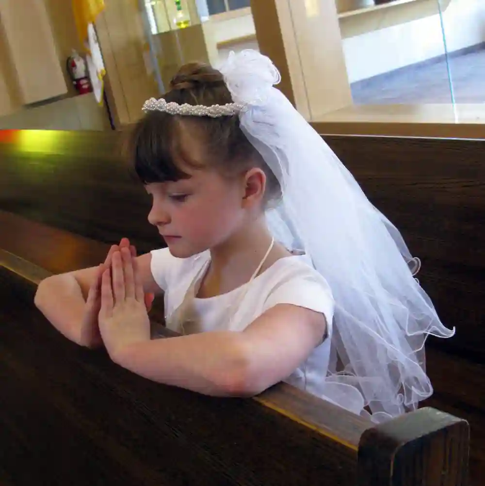 First Communion Girl Wearing Dress and Veil, Praying in Church