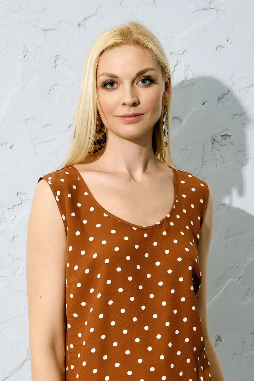 Fashionable blonde woman standing indoors in sleeveless blouse